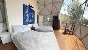 A bedroom with two beds, a painting, a TV, and a small table with chairs. - Glamping Cholula (San Pedro Cholula)
