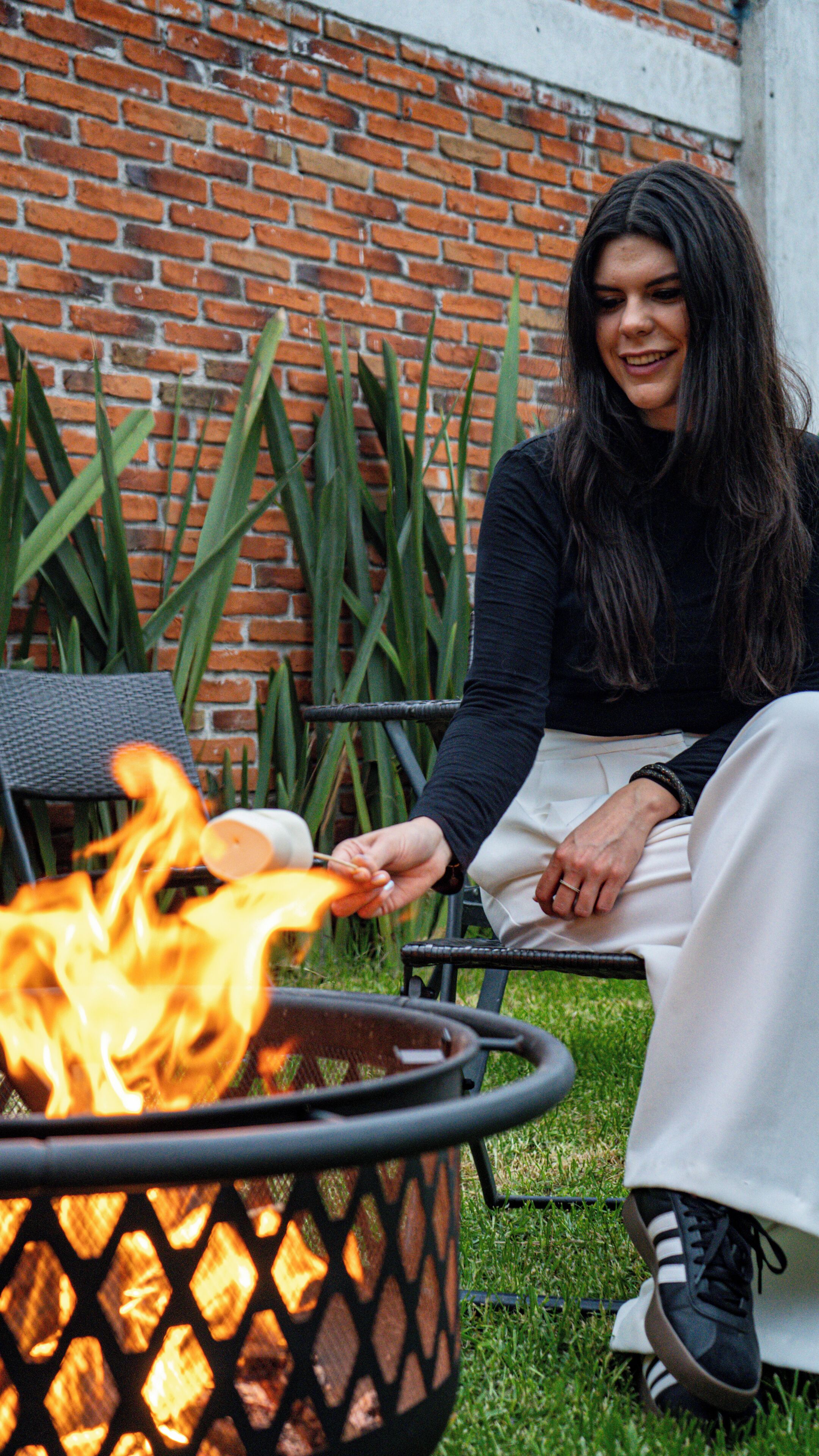 A person sitting by a fire pit with a brick wall in the background.