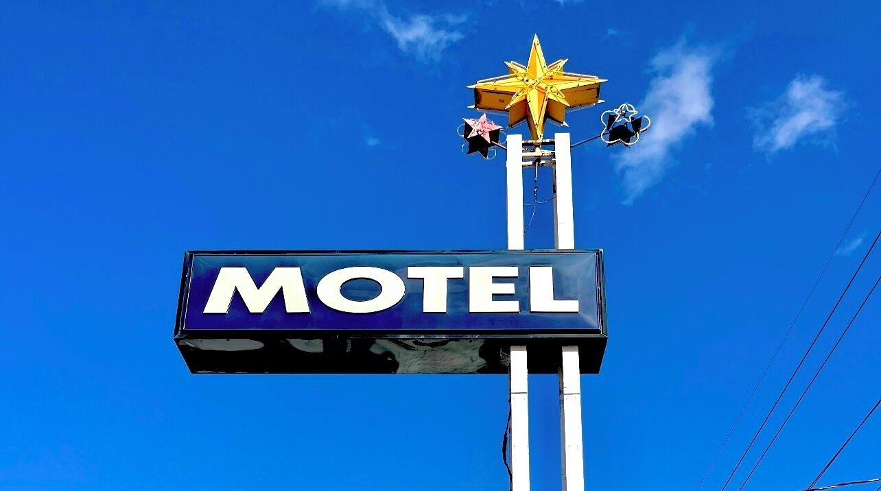 A motel sign with a star and a 'MOTEL' signboard against a clear blue sky.