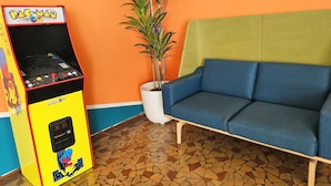 Een Pac-Man automaat, een blauwe bank en een potplant in een kamer met oranje en blauwe muren en een mozaïek vloer.