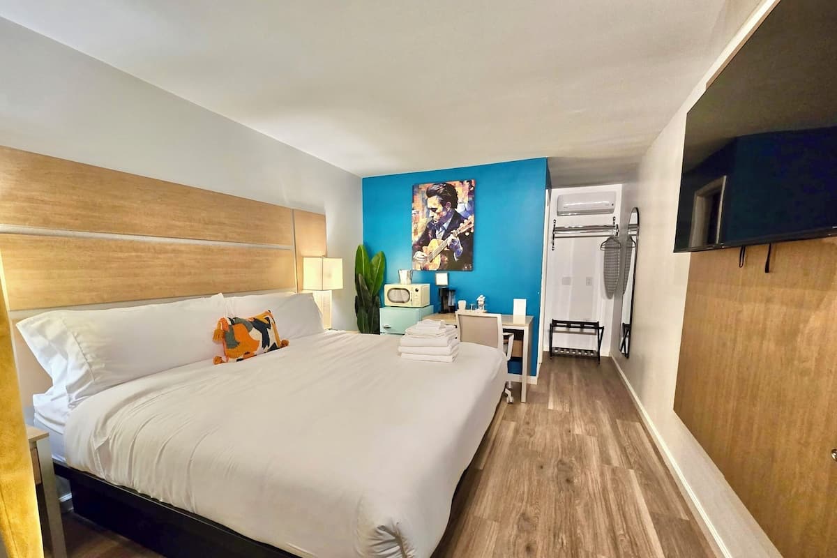 A hotel room with a large bed, a desk, a chair, a TV, and a wardrobe.