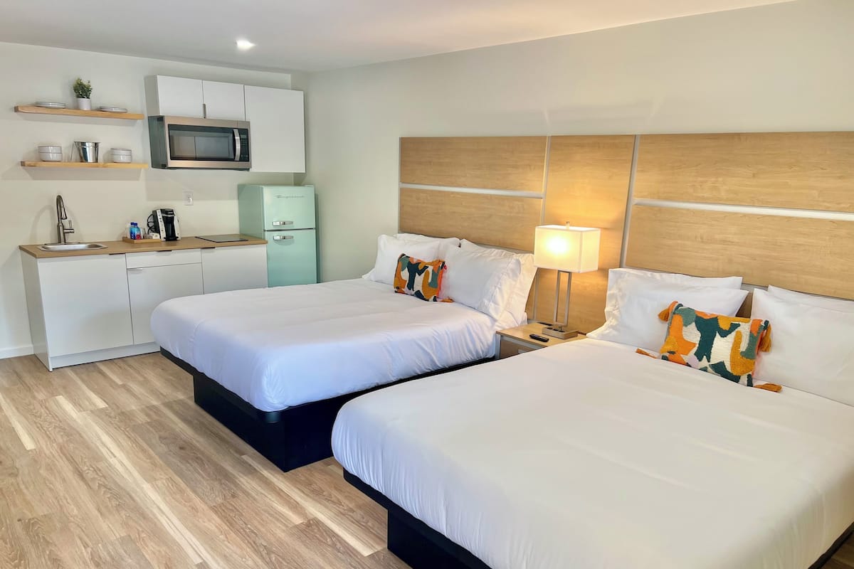 A hotel room with two beds, a kitchenette, and a wooden headboard.