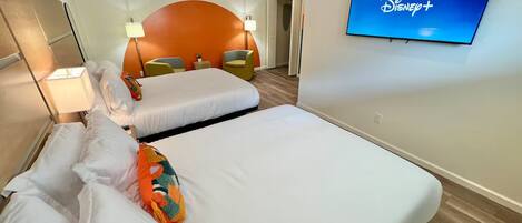 Ein Hotelzimmer mit zwei Betten, einem Fernseher, der das Disney+-Logo zeigt, und einer gewölbten, orangefarbenen Wand.