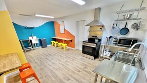 Een moderne keuken met een roestvrijstalen spoelbak, een oven, een magnetron en een fornuis. Er staan gele krukken bij een tafel met een stoel.