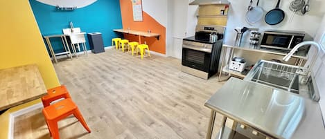 A modern kitchen with a stainless steel sink, an oven, a microwave, and a stove. There are yellow stools and a table with a chair.