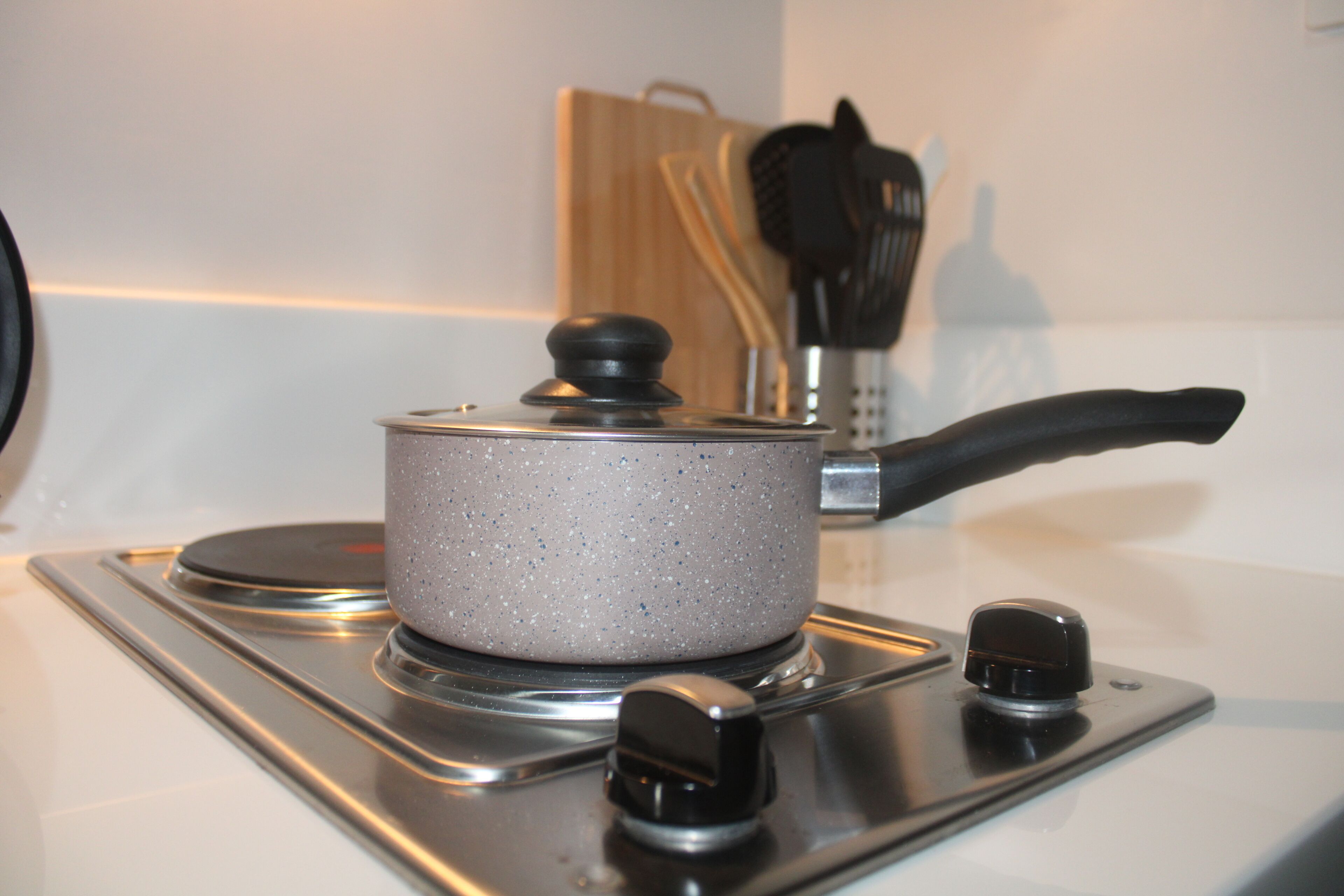 A kitchen stove with a pot on it, a knife block, and a wooden cutting board in the background.