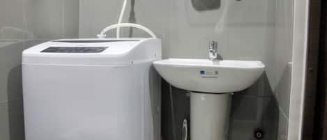 A bathroom with a white water heater, a sink, and a glass shelf with a potted plant.