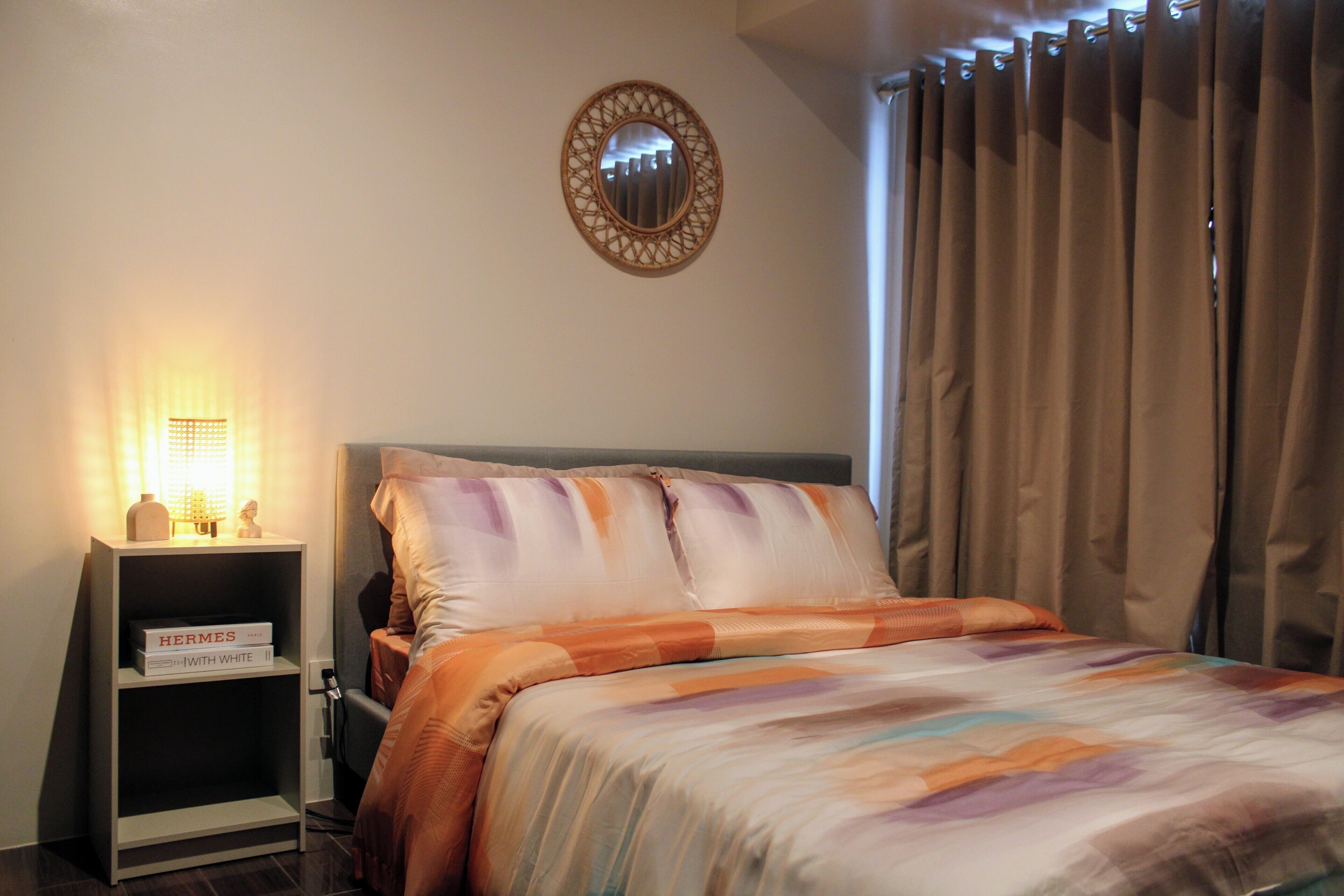 A neatly made bed with a patterned bedspread, a bedside lamp, and a shelf with books.