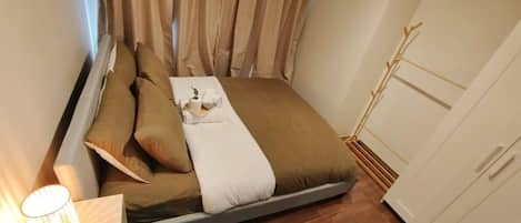 A compact bedroom with a bed, pillows, a bedside lamp, and a wardrobe.