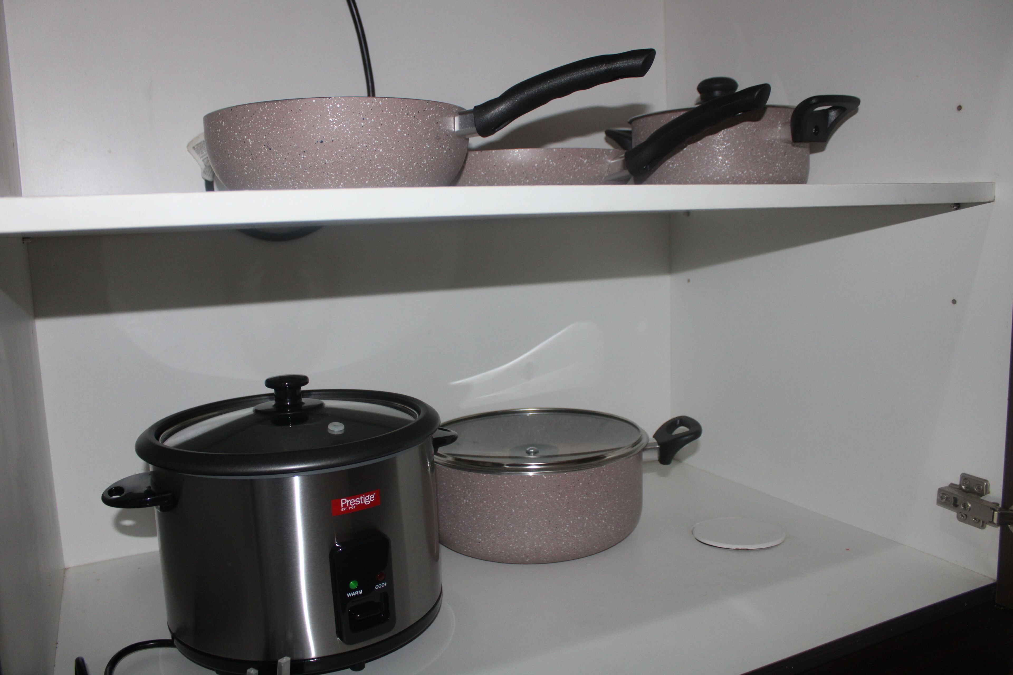 A kitchen with a stainless steel slow cooker, a pink non-stick pot, and a white plate on a white shelf.