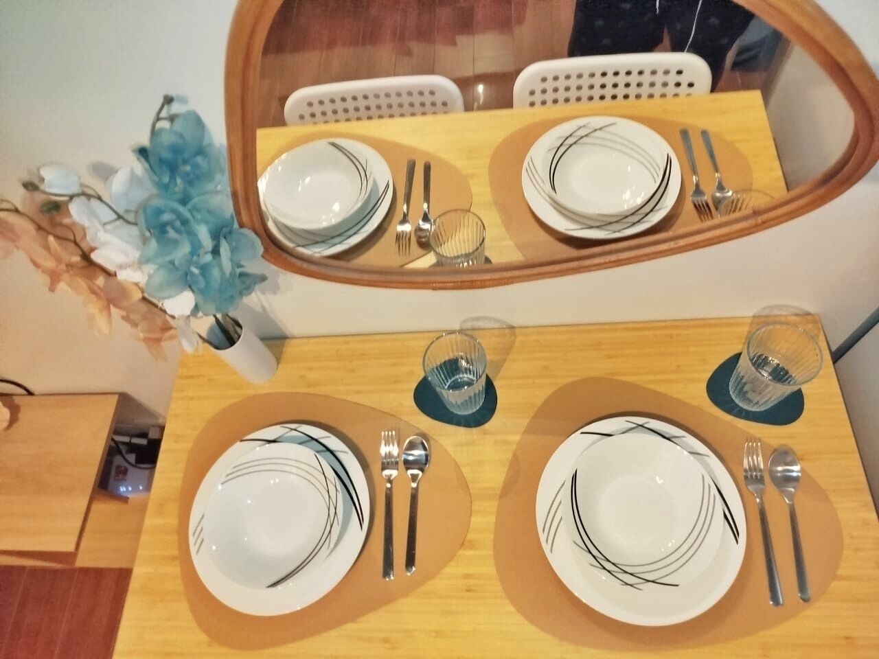 Una mesa de comedor dispuesta con platos, cubiertos y copas, que se reflejan en un espejo de arriba.