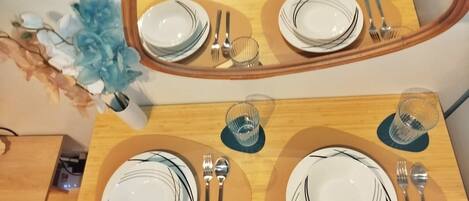 Una mesa de comedor dispuesta con platos, cubiertos y copas, que se reflejan en un espejo de arriba.