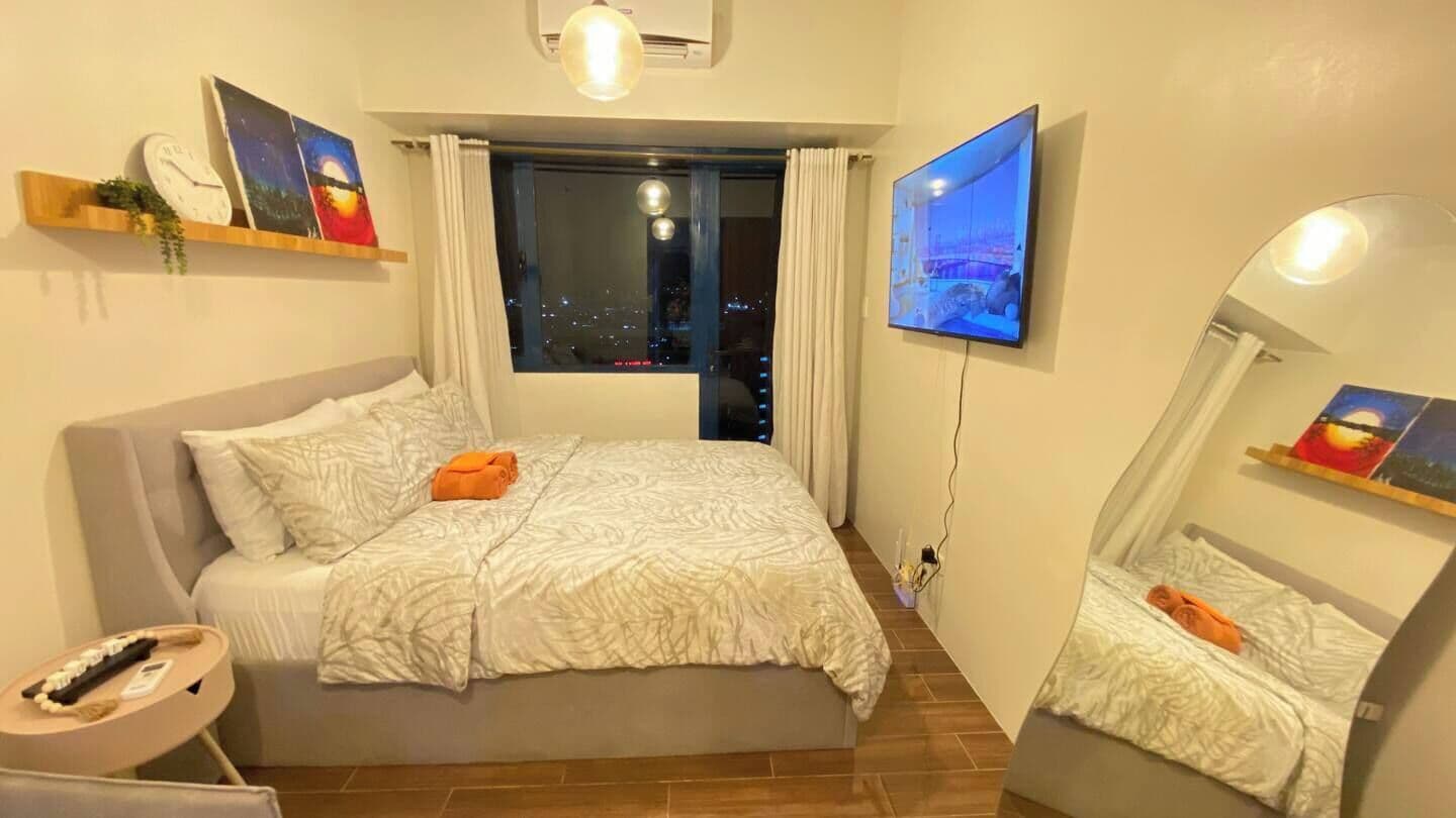 A modern bedroom with a bed, a TV, a bedside table, and a window with curtains.