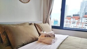 A hotel room with a bed, pillows, a tray with towels and a small plant, and a view of buildings through the window. - Air Residences-CBD view  (Makati)