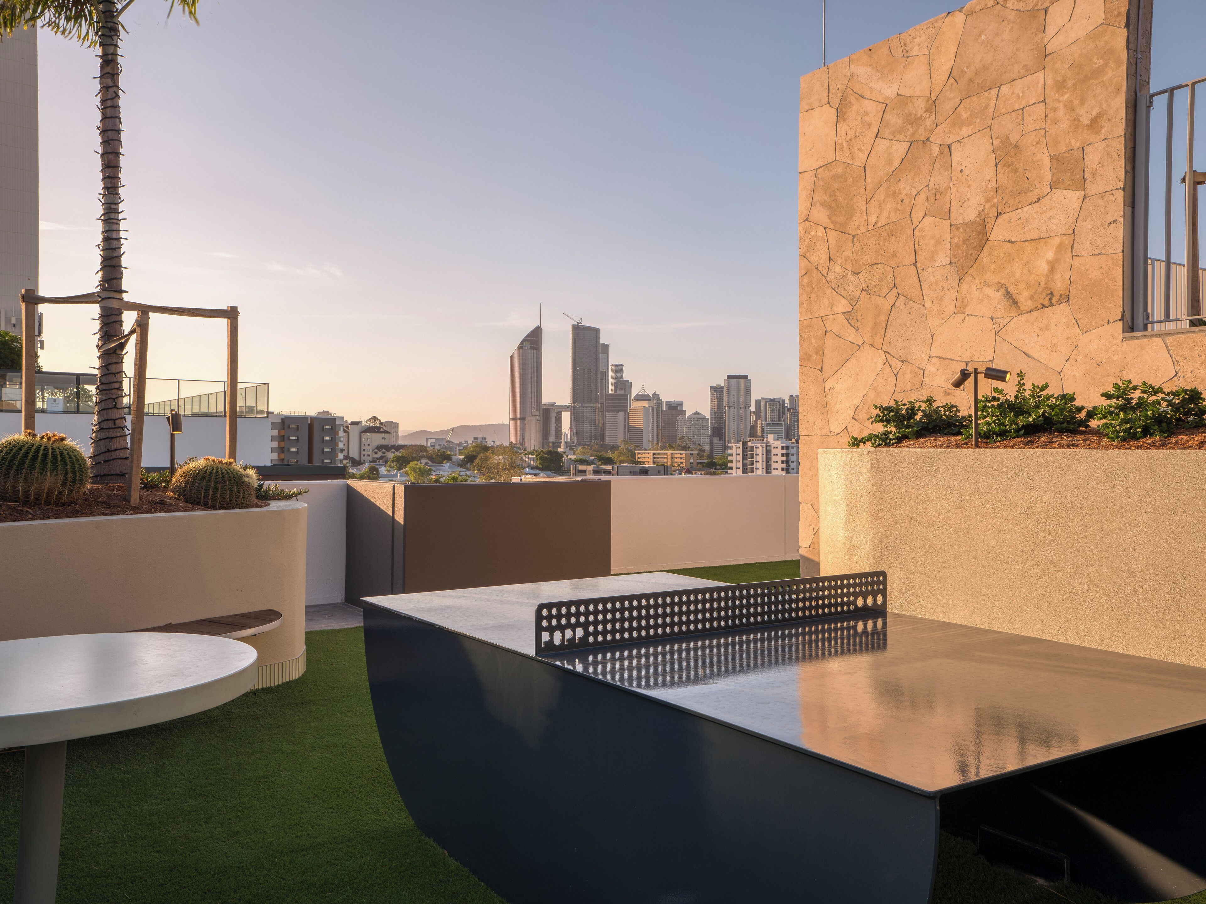 A rooftop terrace with a modern table, a palm tree, and a city skyline view.