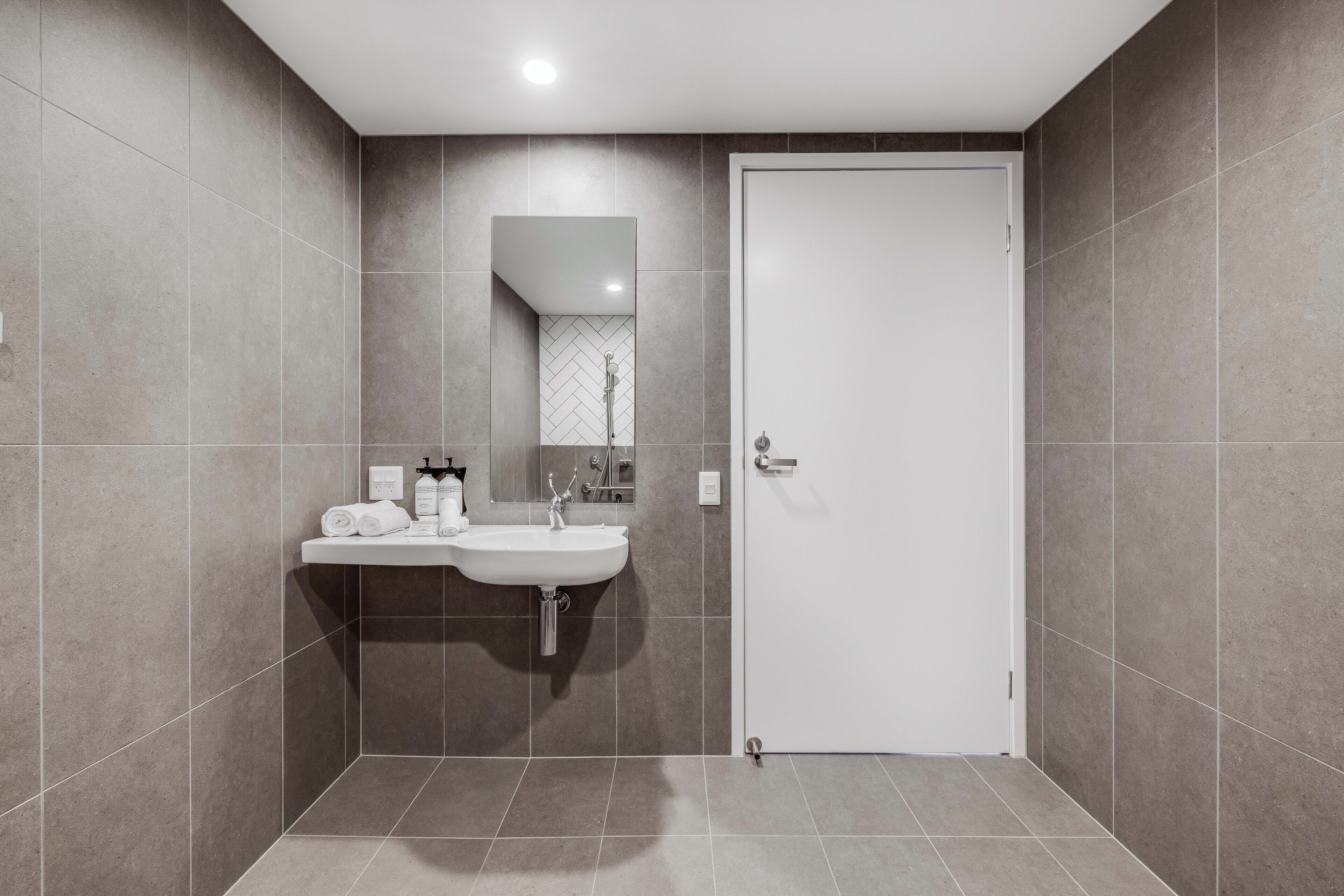 Un baño moderno con un lavamanos, espejo y puerta blancos.