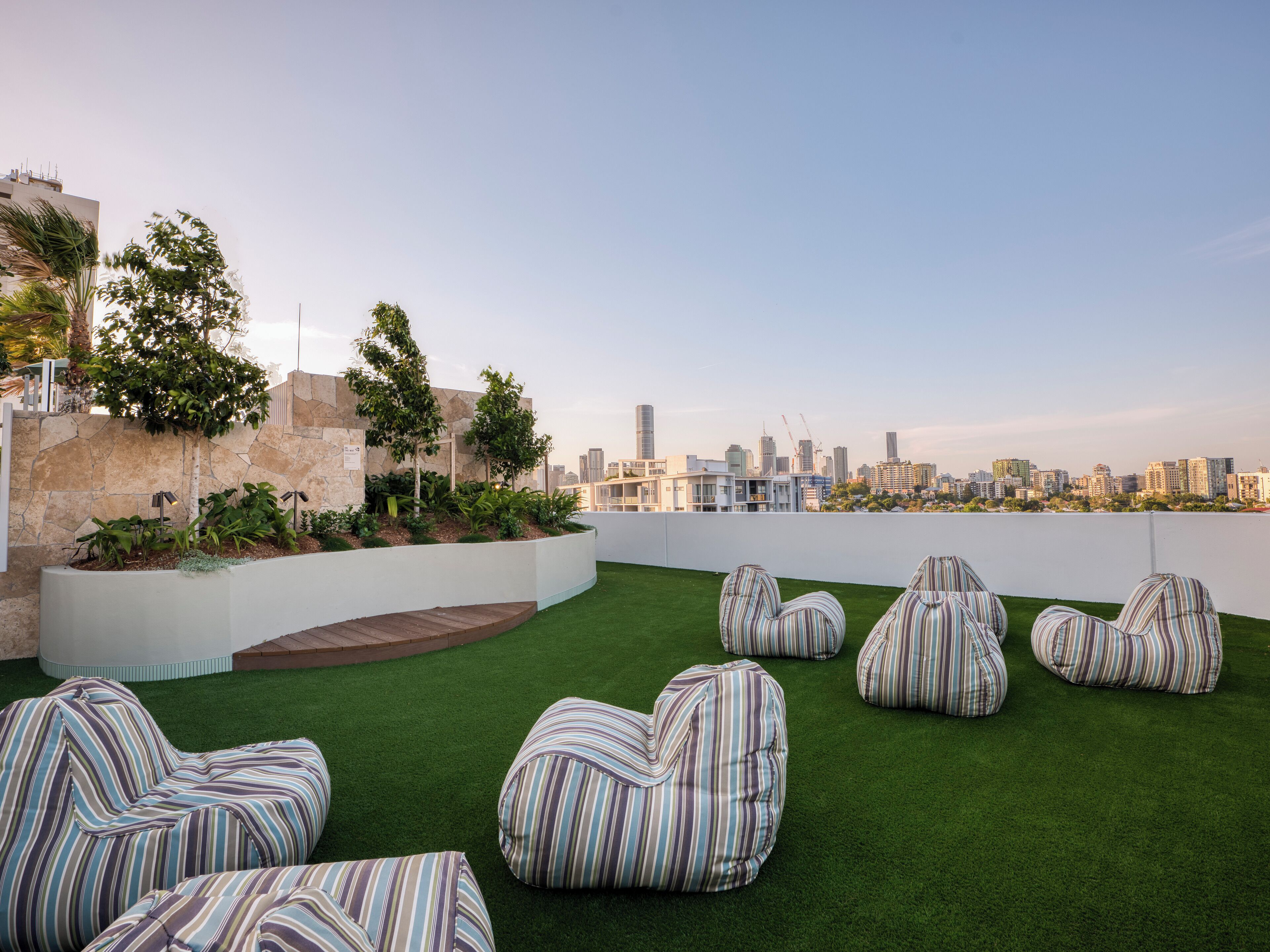 A rooftop terrace with green artificial turf, striped bean bag chairs, and a city skyline view.