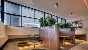 A modern lobby with a seating area, a wooden planter with plants, and a large window providing a view of the outside. - Rambla @ Story House (Kangaroo Point)