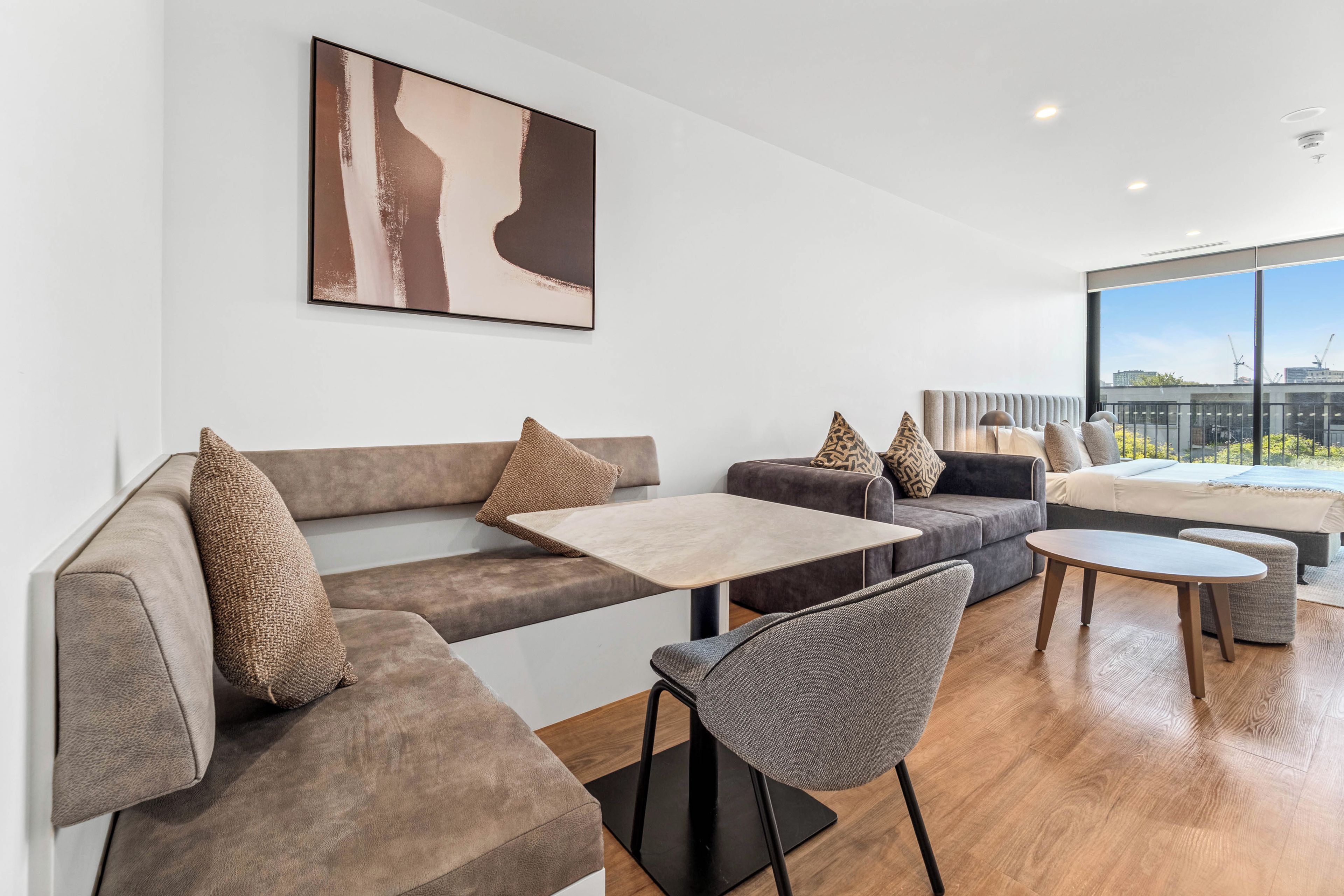 A modern living room with a sofa, chairs, a coffee table, and a large window offering a view of the city.