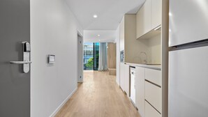 A modern kitchen with white cabinets, a stainless steel refrigerator, and a wooden floor. - Rambla @ Story House (Kangaroo Point)