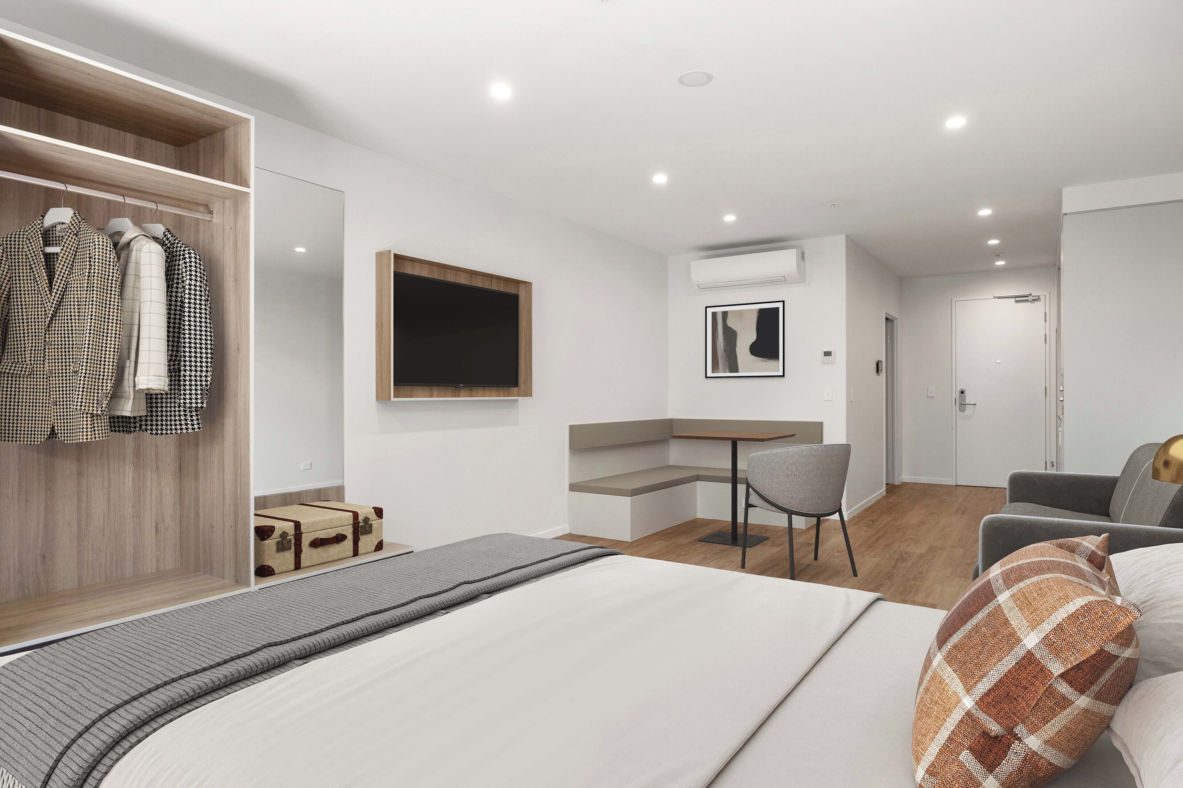 Une chambre d’hôtel moderne comprenant un lit, un coin salon avec une table et des chaises, une armoire avec des vêtements suspendus et un téléviseur.