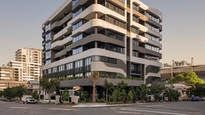 Un edificio de varios pisos con fachada curva, balcones y un estacionamiento con coches.