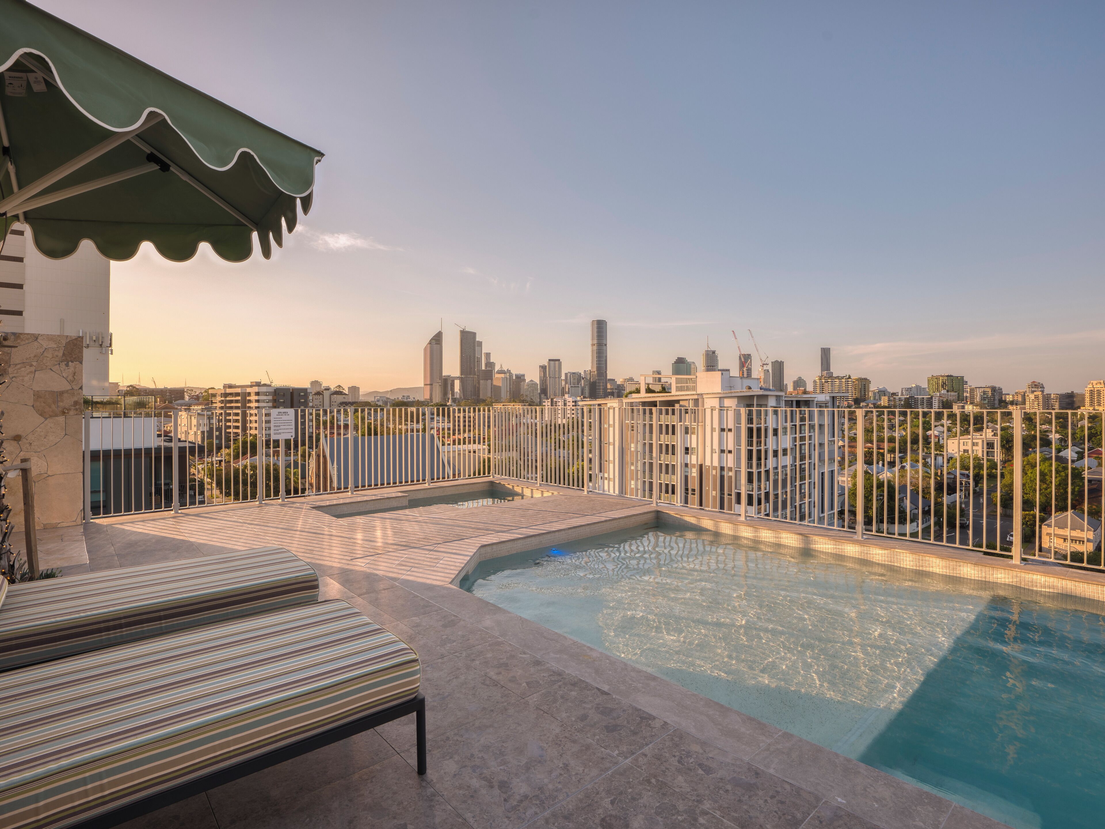 Una piscina en la azotea con sillones de descanso, vista al horizonte de la ciudad y un toldo verde.