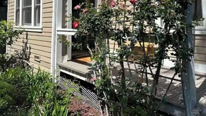 Ein Haus mit überdachter Veranda, einem Fenster und einem Garten mit Pflanzen und Blumen.