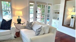 Ein Wohnzimmer mit einem weißen Sofa, gemusterten Kissen, einer Lampe und einem großen Spiegel.