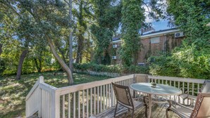 A wooden deck with a table and chairs, surrounded by trees and a brick building. - Lovely Beach House -Ocean Duplex (Norfolk)