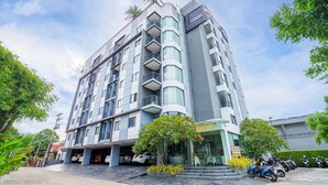 Et hotel i flere etager med et moderne design, med altaner på hver etage, parkeringsplads under tag og et tydeligt skilt med hotellets navn.