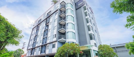 Un hôtel à plusieurs étages au design moderne, doté de balcons à chaque niveau, d’un parking couvert et d’une enseigne bien visible.