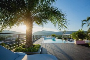Une piscine sur le toit offrant une vue sur les montagnes, entourée de palmiers et de chaises longues.