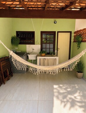 Una hamaca en una habitación con piso de baldosas, una ventana, una puerta y una pequeña mesa con una planta.