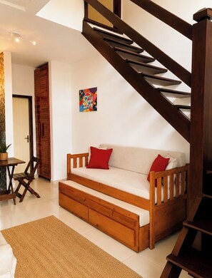 A modern living room with a wooden staircase, a sofa with cushions, a small table with chairs, and a colorful artwork on the wall. - Cozy and family atmosphere (Paraty)