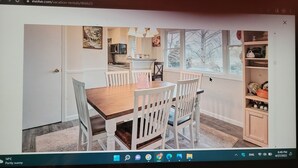 A room with a wooden dining table, white chairs, a kitchen area with a microwave, and a window with a view of trees. - confortable villa (New Carrollton)