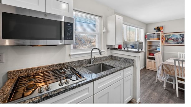 A modern kitchen with white cabinetry, a stainless steel microwave, a gas stove, and a granite countertop. - confortable villa (New Carrollton)