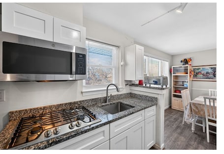 A modern kitchen with white cabinetry, a stainless steel microwave, a gas stove, and a granite countertop.