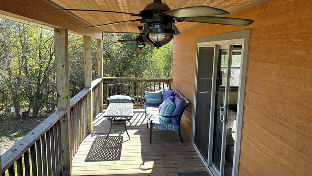 Une terrasse en bois dotée d’un ventilateur de plafond, d’une porte-fenêtre coulissante et d’un espace salon extérieur avec des coussins.
