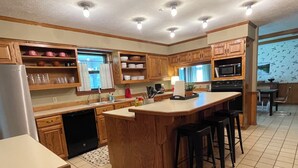 A kitchen with wooden cabinets, a central island with bar stools, a dishwasher, and a microwave. - Cozy 3-bedroom house in Meridian (Meridian)