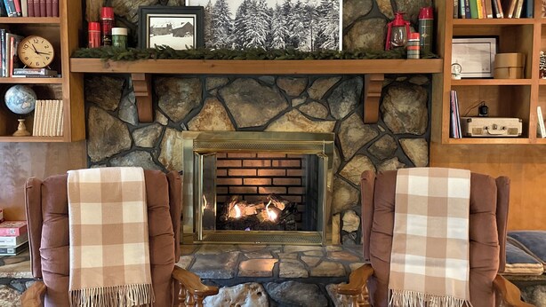 A cozy living room with a stone fireplace, two armchairs, and bookshelves filled with books and decorative items. - Cozy 3-bedroom house in Meridian (Meridian)