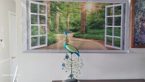 A room with a large window displaying a forest scene, a peacock decoration, and a lamp. - Comfortable villa (New Carrollton)