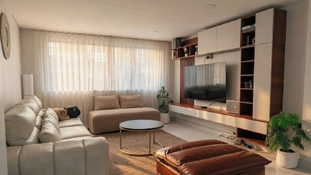 Una sala de estar moderna con sofá, reposapiés, mesa de centro y mueble para televisión.