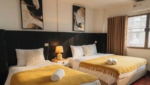 Habitación de hotel con dos camas, piso de madera, cabecera negra y obras de arte en las paredes.