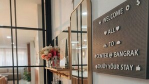 Un área de recepción con un cartel de bienvenida, un espejo, un banco y un arreglo floral.