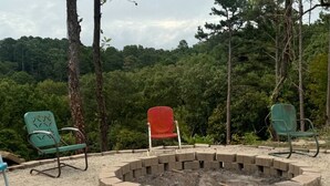 A circular fire pit surrounded by a brick border, with two green chairs and a red chair in the foreground. - RT 62 Motor Resort '50's Cabin w/Jacuzzi (Eureka Springs)