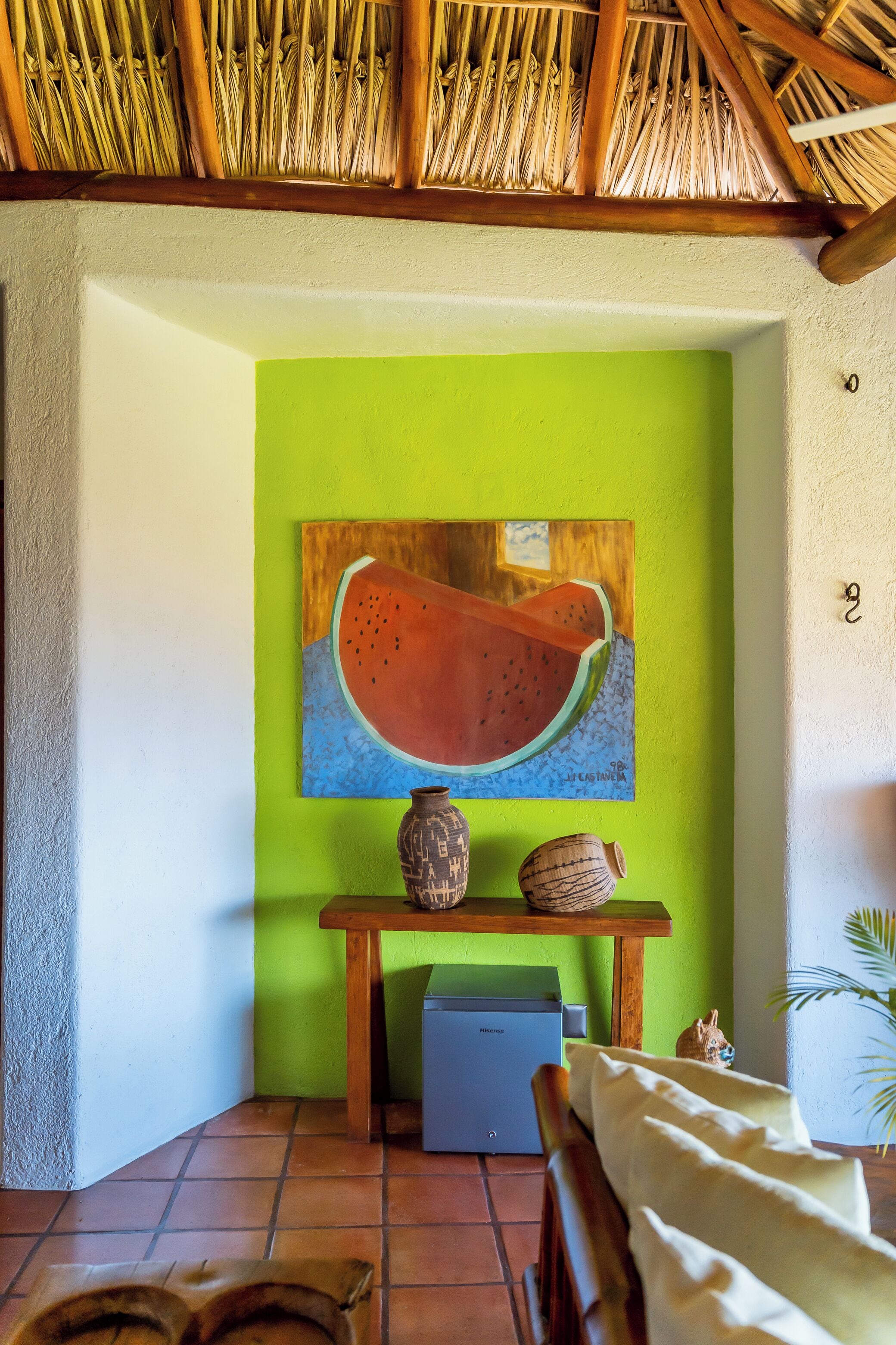 Una habitación con una pared verde, un cuadro de sandía, una mesita con un jarrón y un armario azul.
