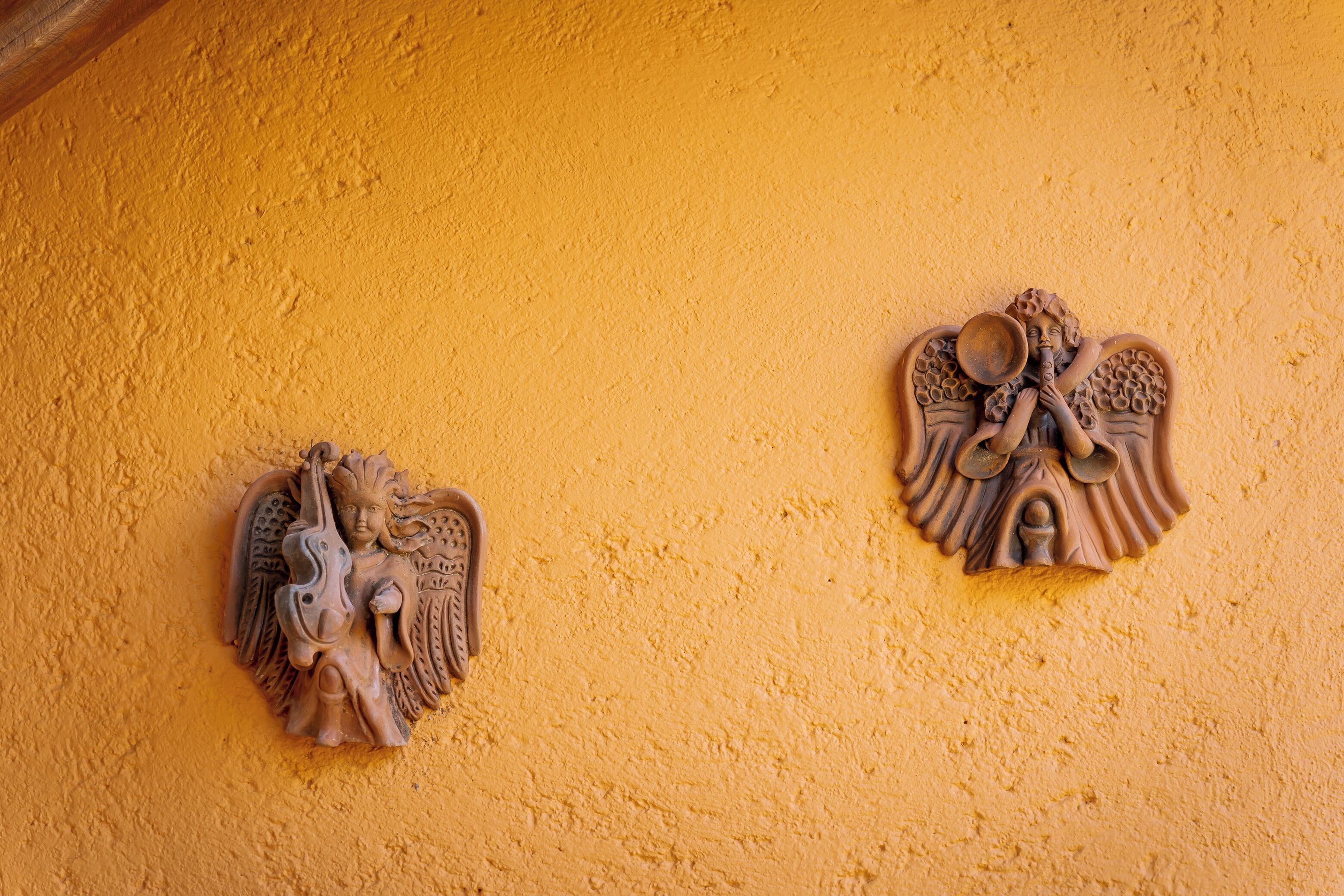 Dos esculturas de ángeles montadas en la pared sobre un muro amarillo con textura.