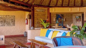 A cozy lounge area with a thatched roof, a sofa with colorful cushions, and a wall adorned with a mural.