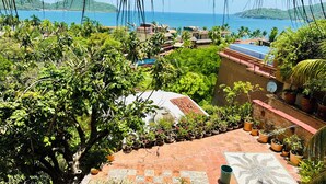 Vue d’une zone côtière avec un jardin en terrasses, des plantes en pot et des bâtiments aux toits recouverts de tuiles rouges.
